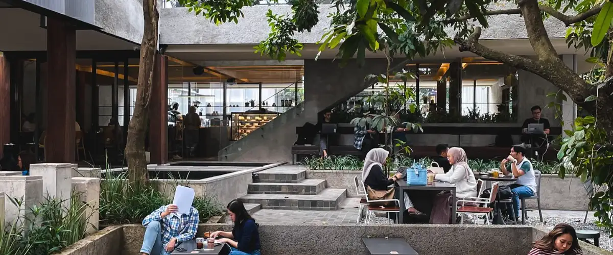 Outdoor café area in Bandung with wooden seating, gravel ground, and lush trees