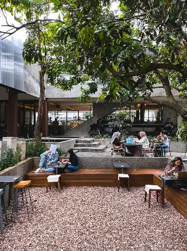 Outdoor café area in Bandung with wooden seating, gravel ground, and lush trees