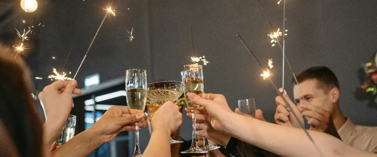 Hands raising a glass and holding a sparkler during a New Year’s Eve celebration.