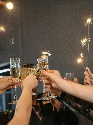Hands raising a glass and holding a sparkler during a New Year’s Eve celebration.