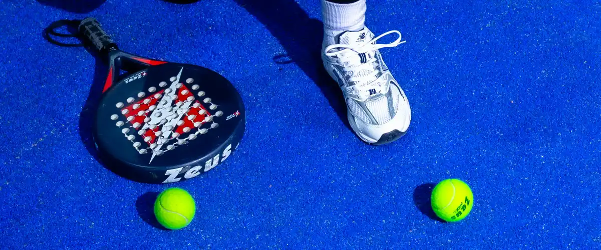 Kneeling player on a blue padel court with racket and balls.