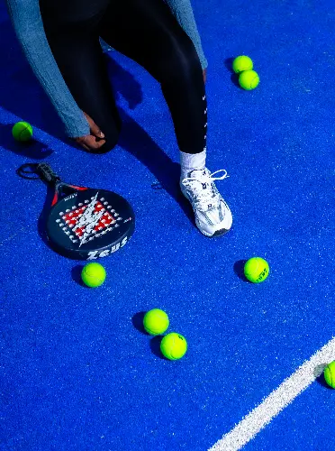 Kneeling player on a blue padel court with racket and balls.