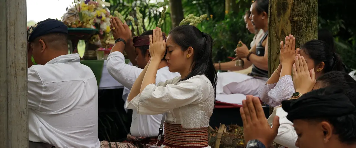 People sitting outdoors in prayer during a ceremonial ritual.