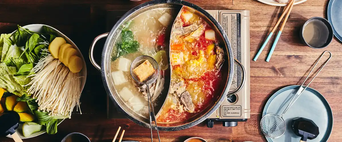 Hotpot with spicy and clear broth surrounded by meat, vegetables, tofu, and noodles.