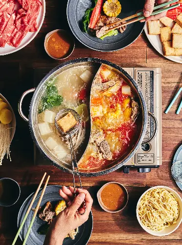 Hotpot with spicy and clear broth surrounded by meat, vegetables, tofu, and noodles.
