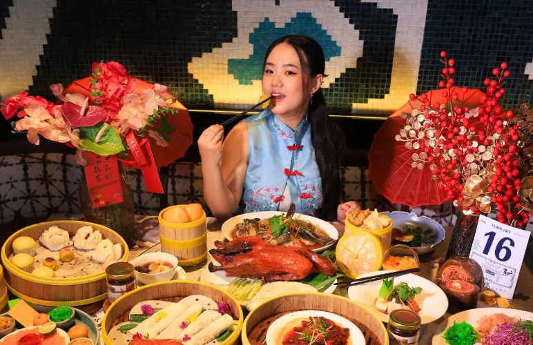 A woman enjoying a Chinese feast with roast duck and dim sum.