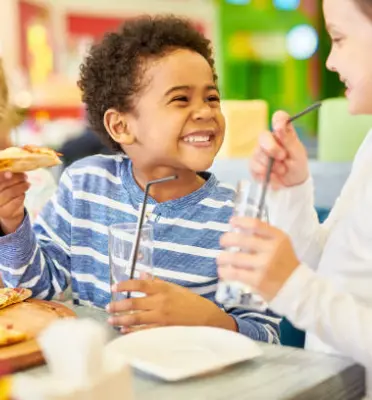 Children laughing and eating pizza at a kid-friendly restaurant.