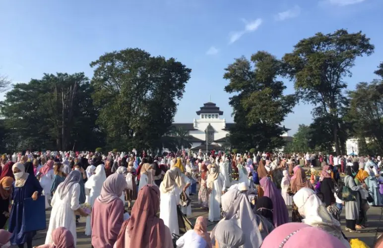 Crowd leaving Eid prayer at Gasibu Field with Gedung Sate in the background.