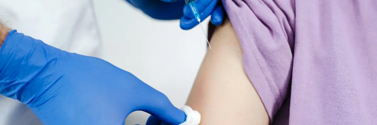 A healthcare worker administering a vaccine injection to a patient’s upper arm.
