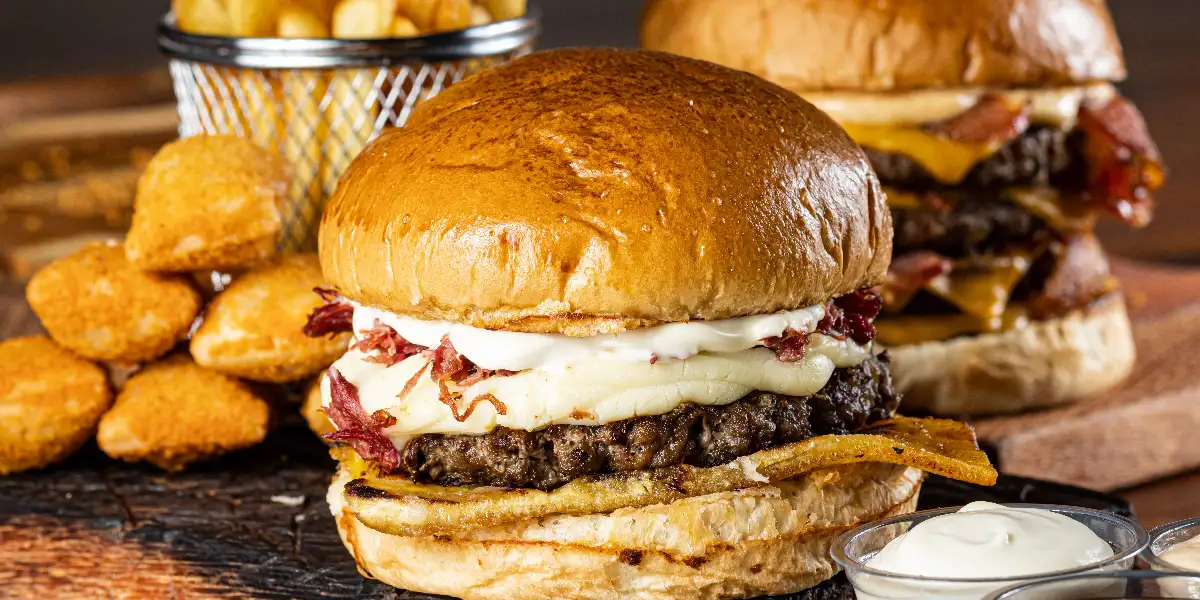 Juicy gourmet burgers with fries and nuggets on a wooden serving board.
