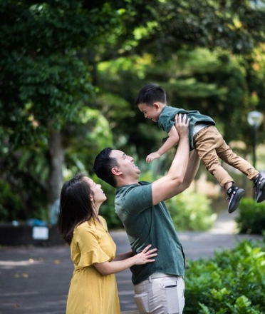 A_father_lifts_his_child_as_the_mother_watches_with_joy
