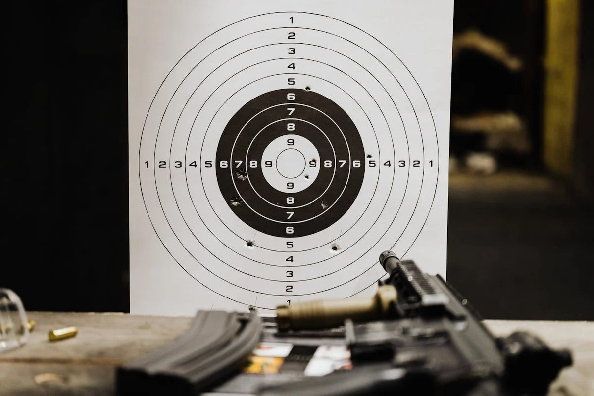 Target board at an indoor shooting range with bullet holes and a firearm in the foreground.