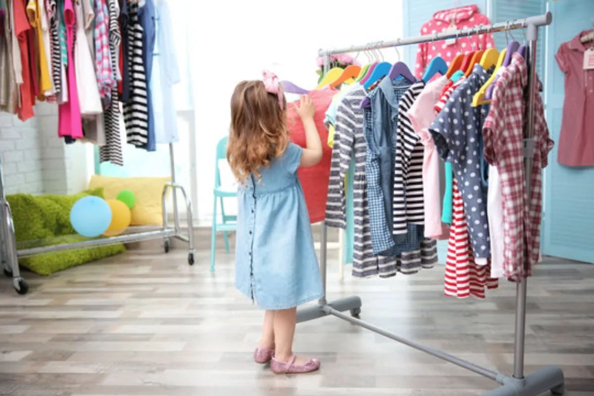 Child browsing colorful kids' clothes on a clothing rack