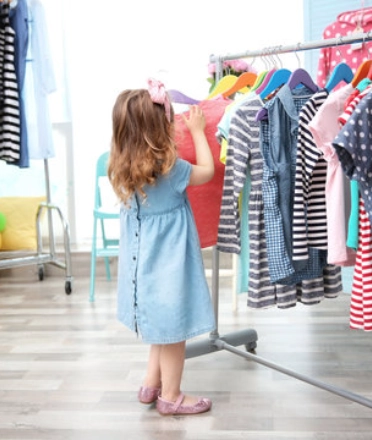 Child browsing colorful kids' clothes on a clothing rack