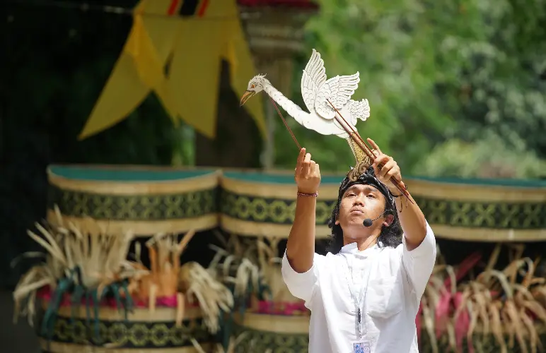 A performer holding a white Balinese shadow puppet during an outdoor cultural presentation 
